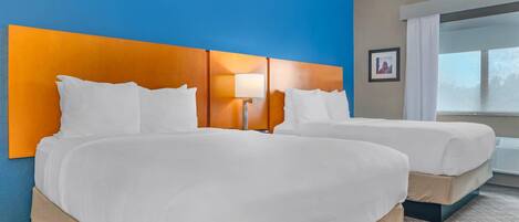 A hotel room with two beds, a blue wall, and a window with curtains.
