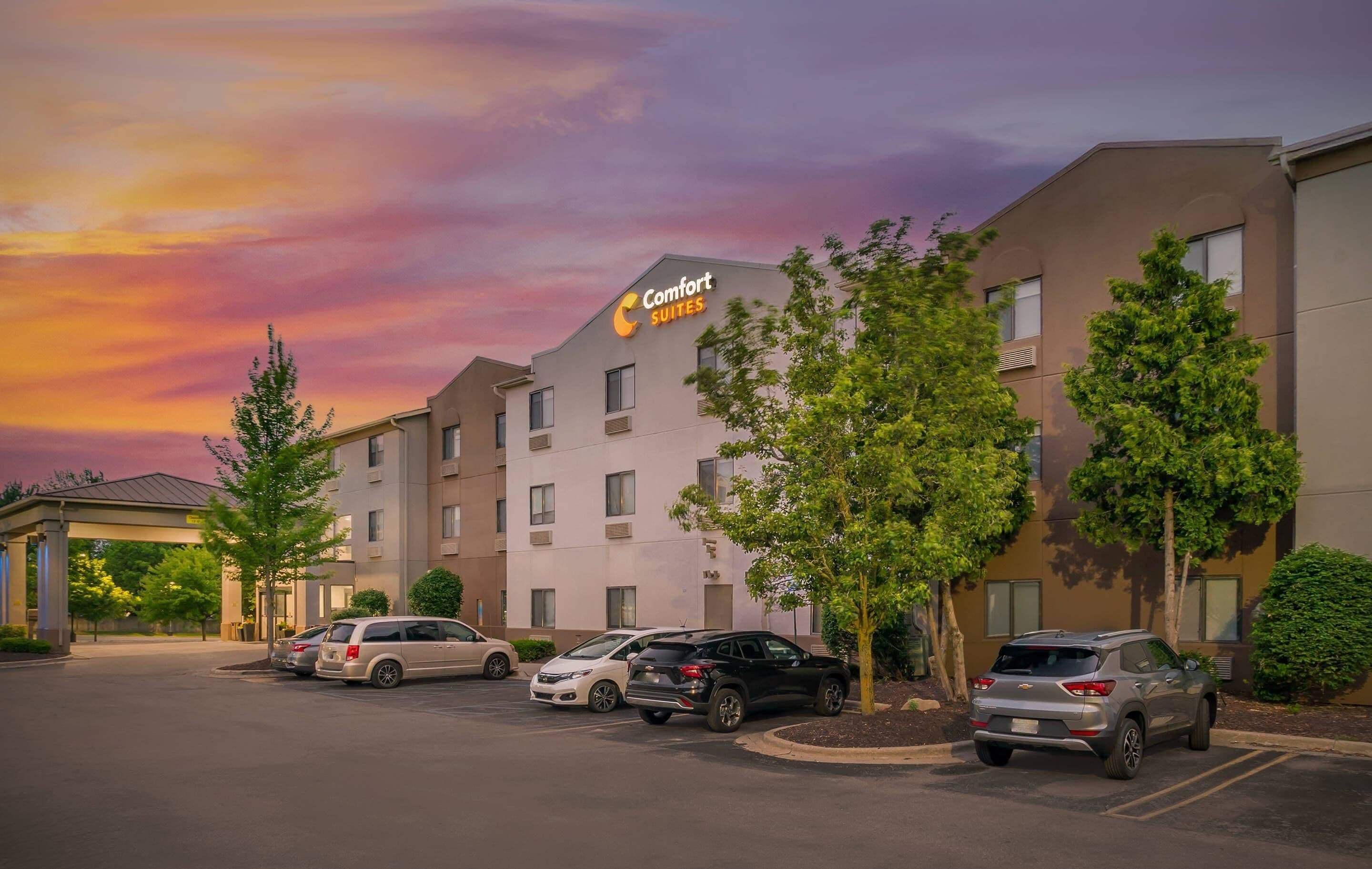 A hotel with a sign reading "Comfort Suites" and a parking lot with several cars.