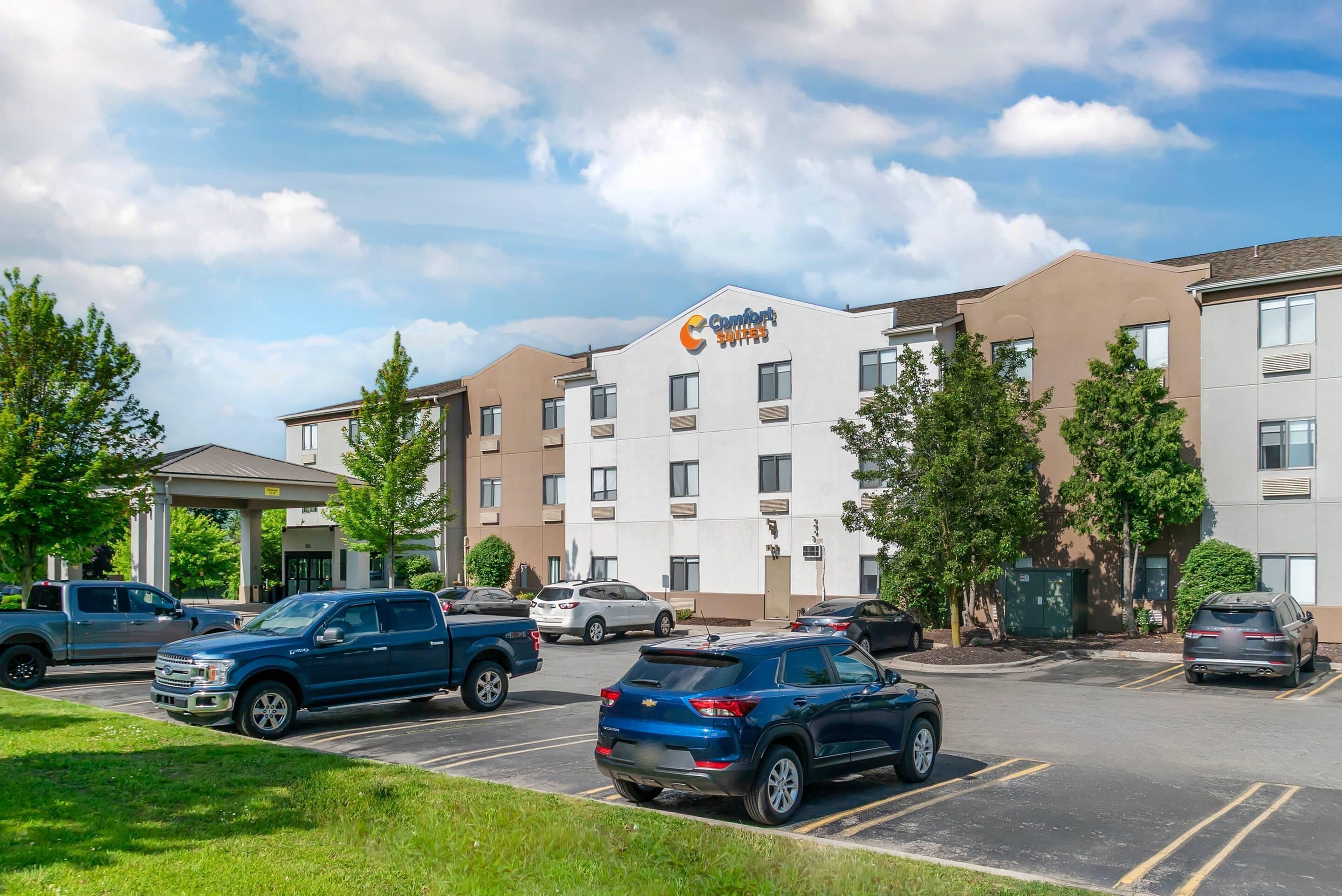 A Comfort Suites hotel with a parking lot, multiple vehicles, and a clear sky.
