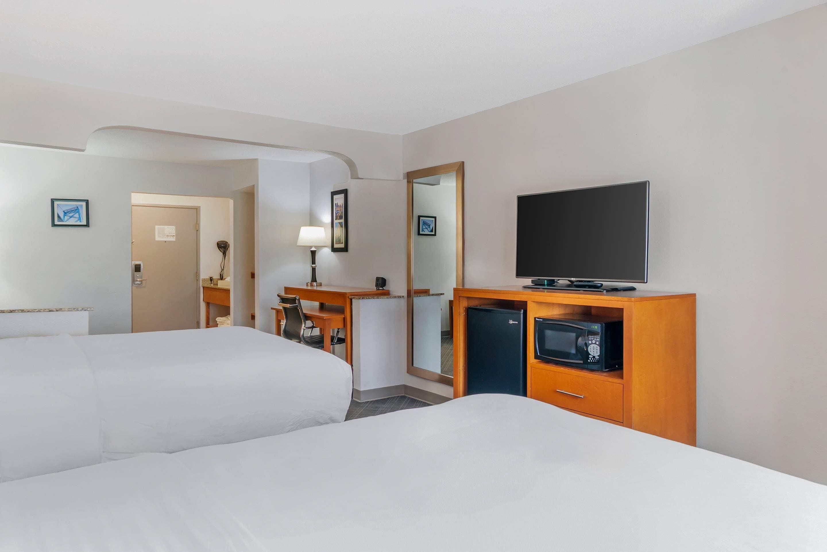 A hotel room with two beds, a desk with a lamp, a television, and a microwave.