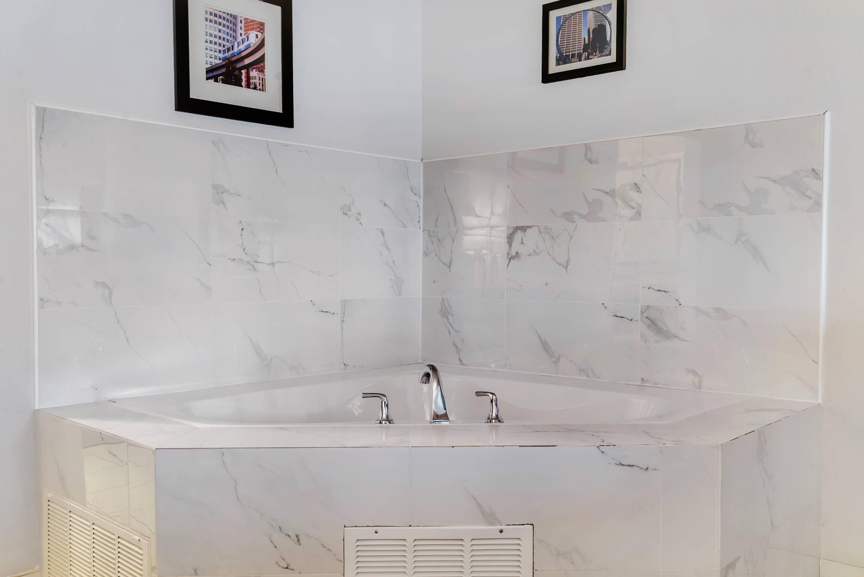 Une salle de bain moderne avec une grande baignoire sur pieds, des carreaux de marbre et deux tableaux encadrés au mur.