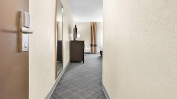 A hotel hallway with a door, a mirror, a cabinet, and a window with curtains.