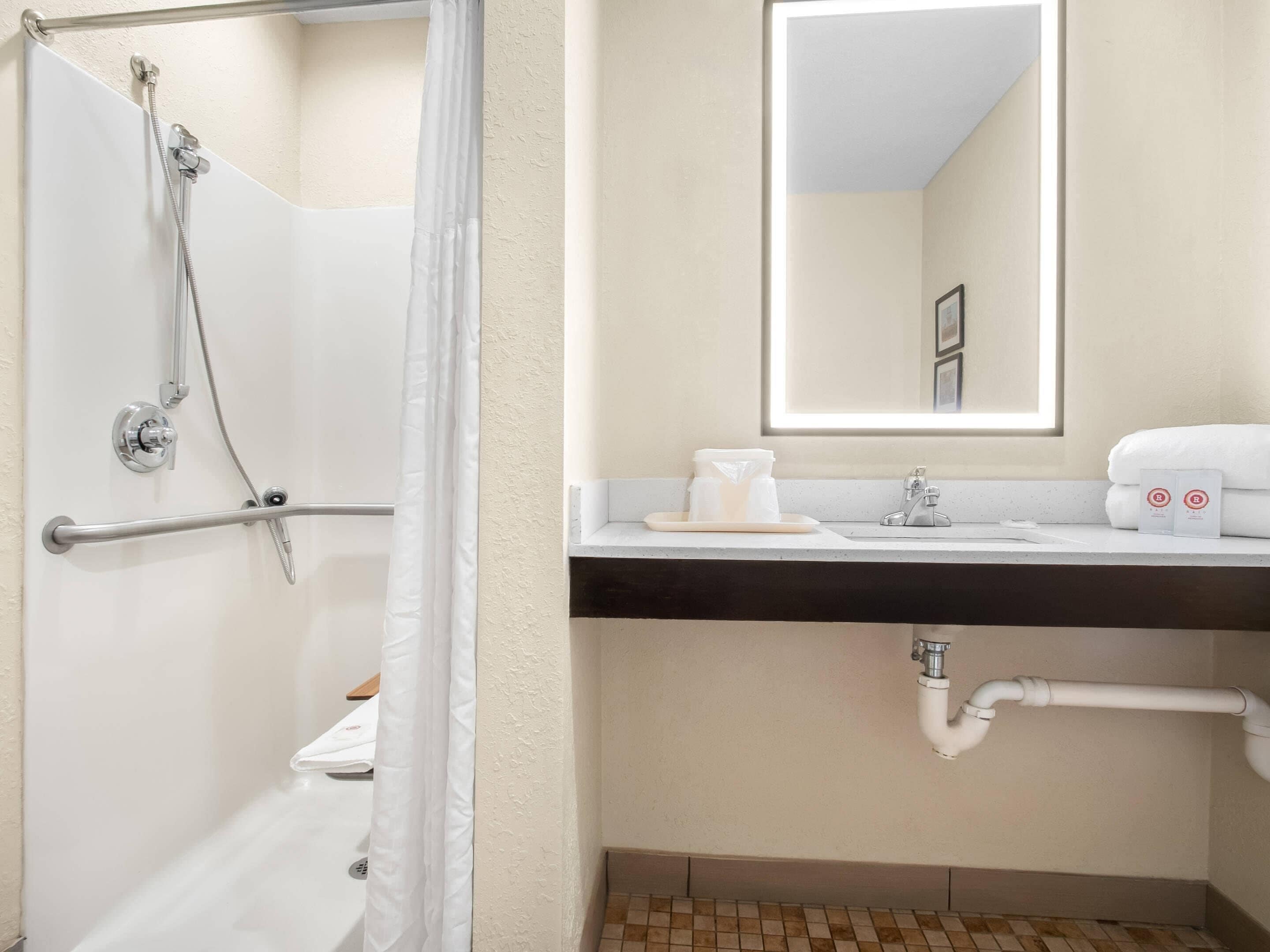 Un baño con ducha, lavabo, espejo y toallero.