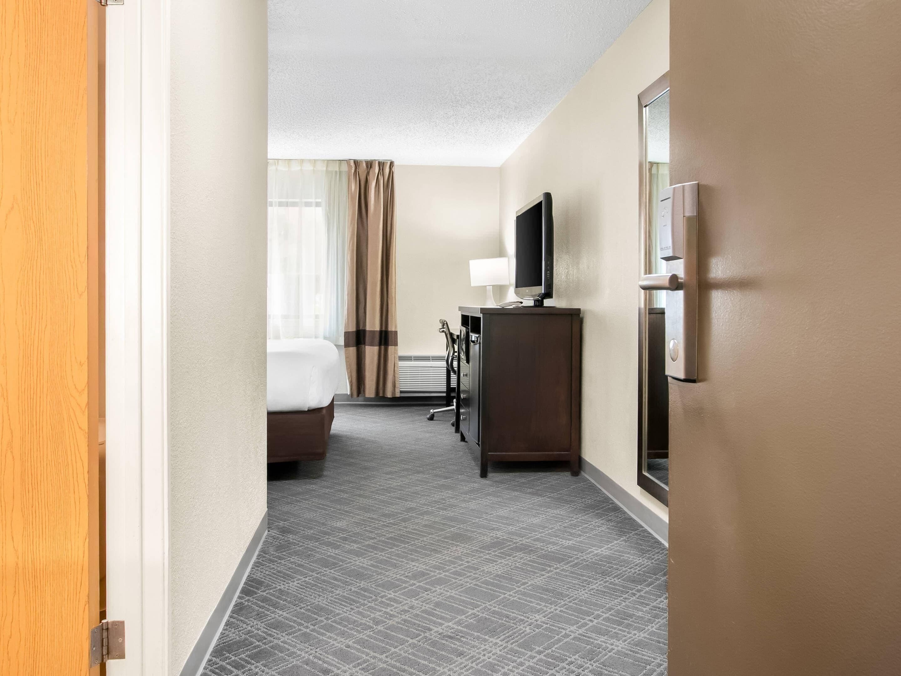A hotel room with a bed, a desk, a television, and a mirror.