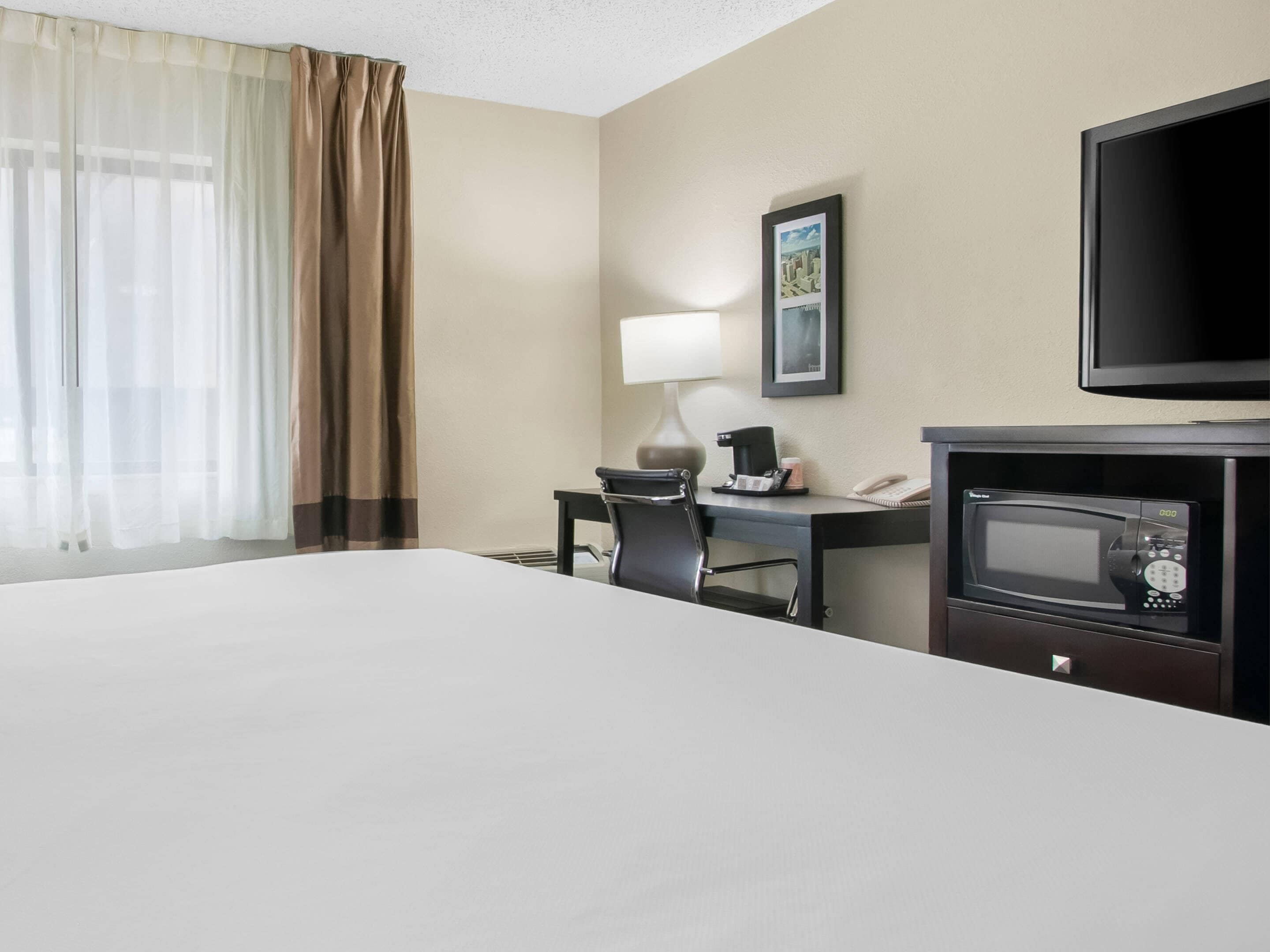 Une chambre d’hôtel équipée d’un lit, d’un bureau avec une chaise, d’une télévision, d’une machine à café et d’un four à micro-ondes.
