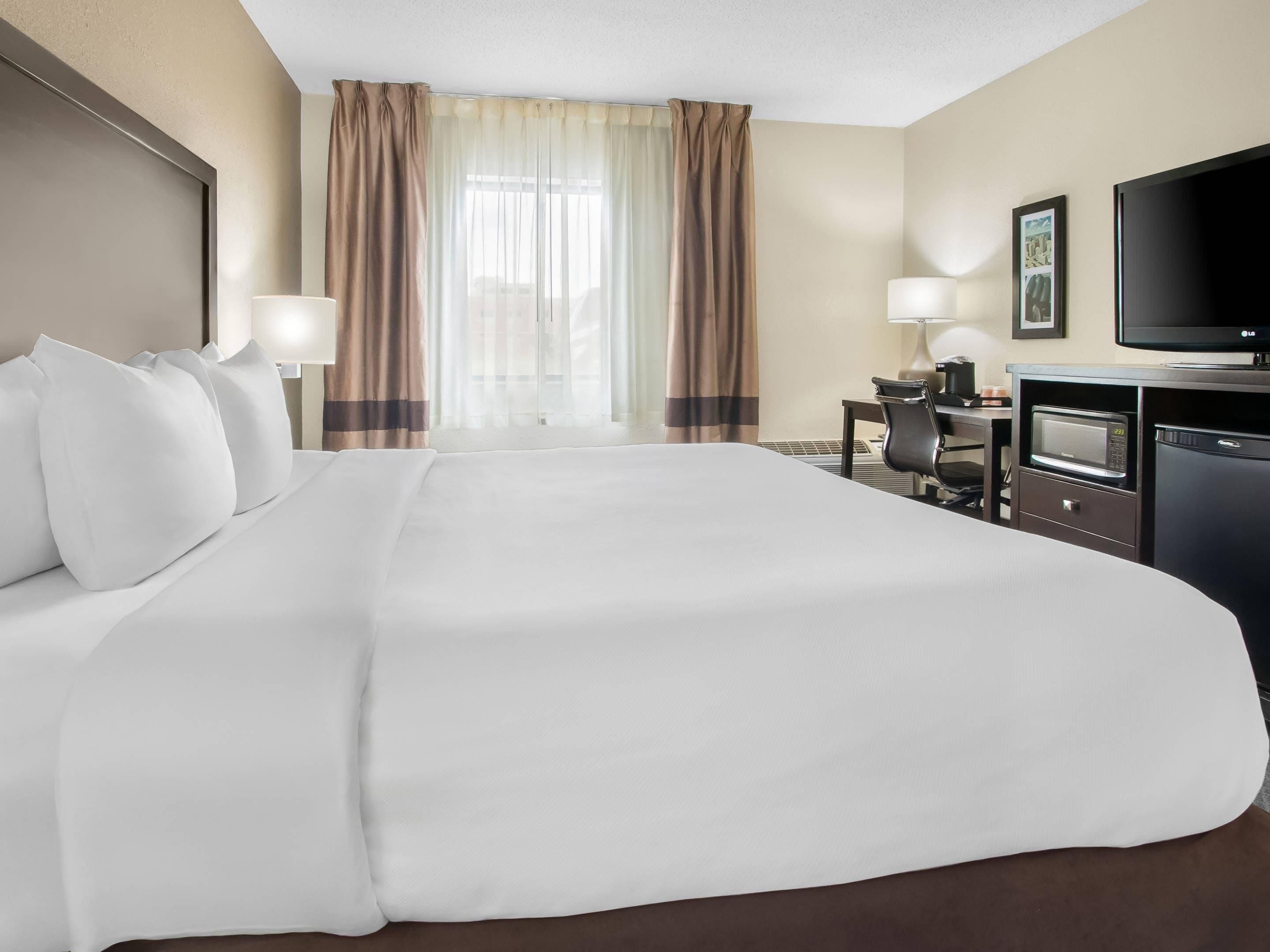 Une chambre d’hôtel avec un grand lit, un bureau avec un ordinateur, une télévision et un four à micro-ondes.