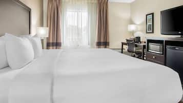Une chambre d’hôtel avec un grand lit, un bureau avec un ordinateur, une télévision et un four à micro-ondes.