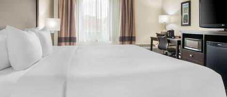A hotel room with a large bed, a desk with a computer, a TV, and a microwave.