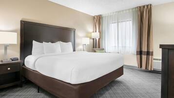 A hotel room with a large bed, two bedside tables, a chair, a desk, and a window with curtains.
