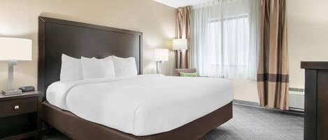 Habitación de hotel con una cama grande, dos mesitas de noche, una silla, un escritorio y una ventana con cortinas.