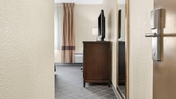 A hotel hallway with a wooden desk, a flat-screen TV, a mirror, and a door with a handle.