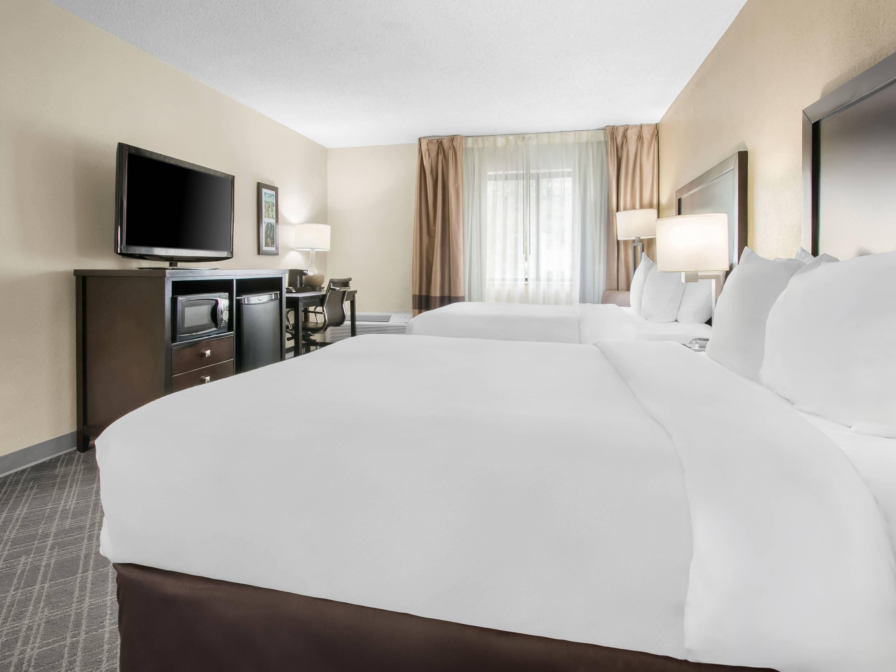 A hotel room with a large bed, a TV, a desk with a chair, and a window with curtains.