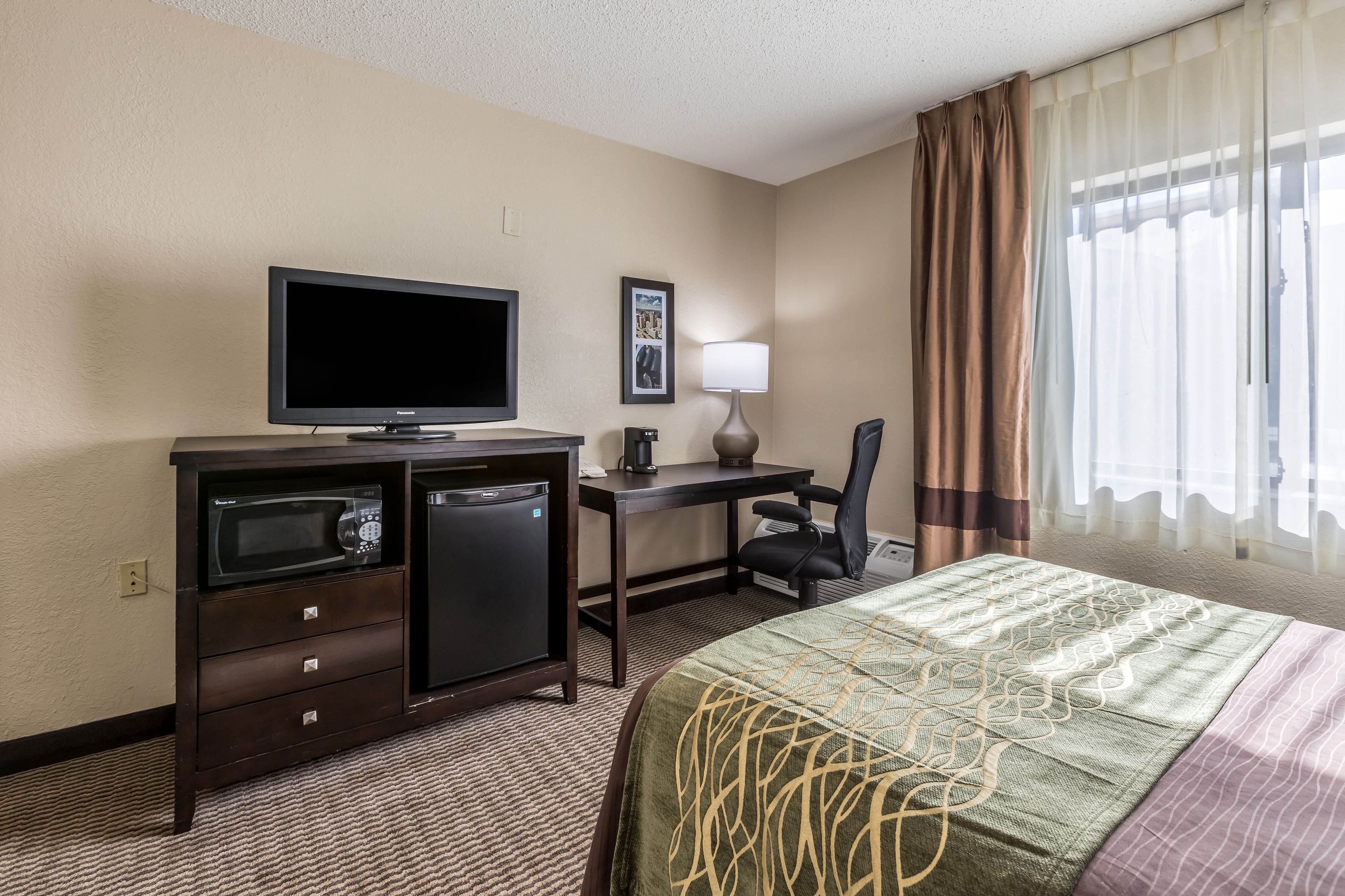 A hotel room with a bed, a desk with a computer, a television, a microwave, and a chair.