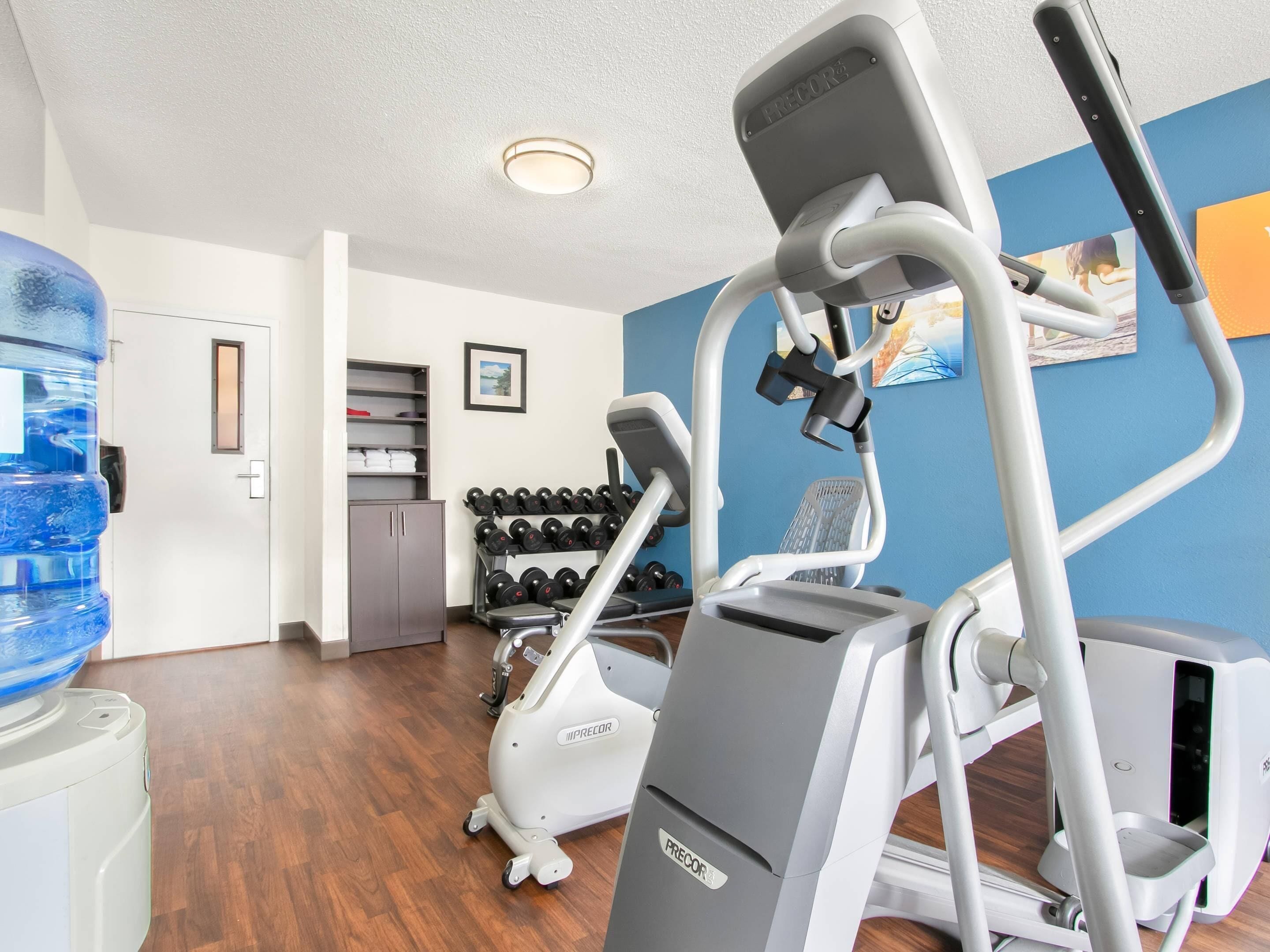A gym with exercise equipment, a water dispenser, and a rack of dumbbells.