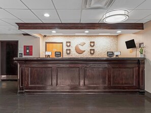 A hotel reception desk with a wooden panel design, a brick wall backdrop, and a mounted television. - Comfort Inn Detroit Downtown (Detroit)