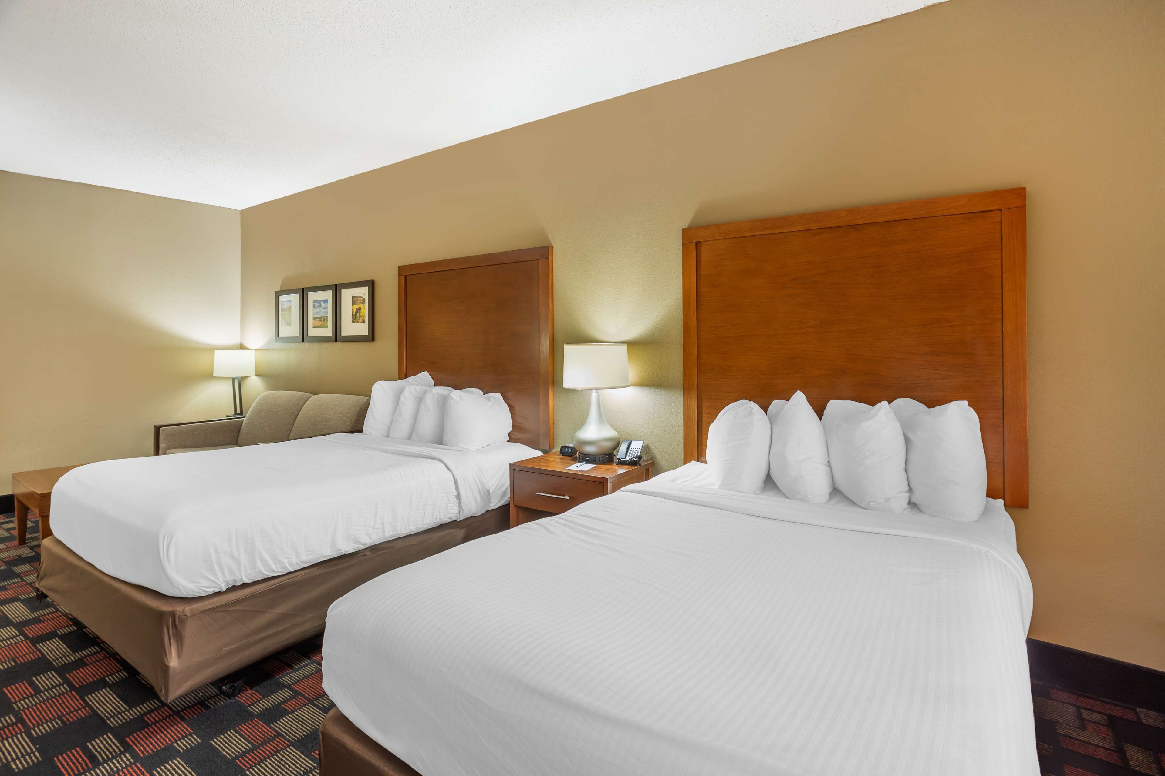 Habitació d'hotel amb dos llits, una tauleta de nit amb una làmpada i una taula petita.