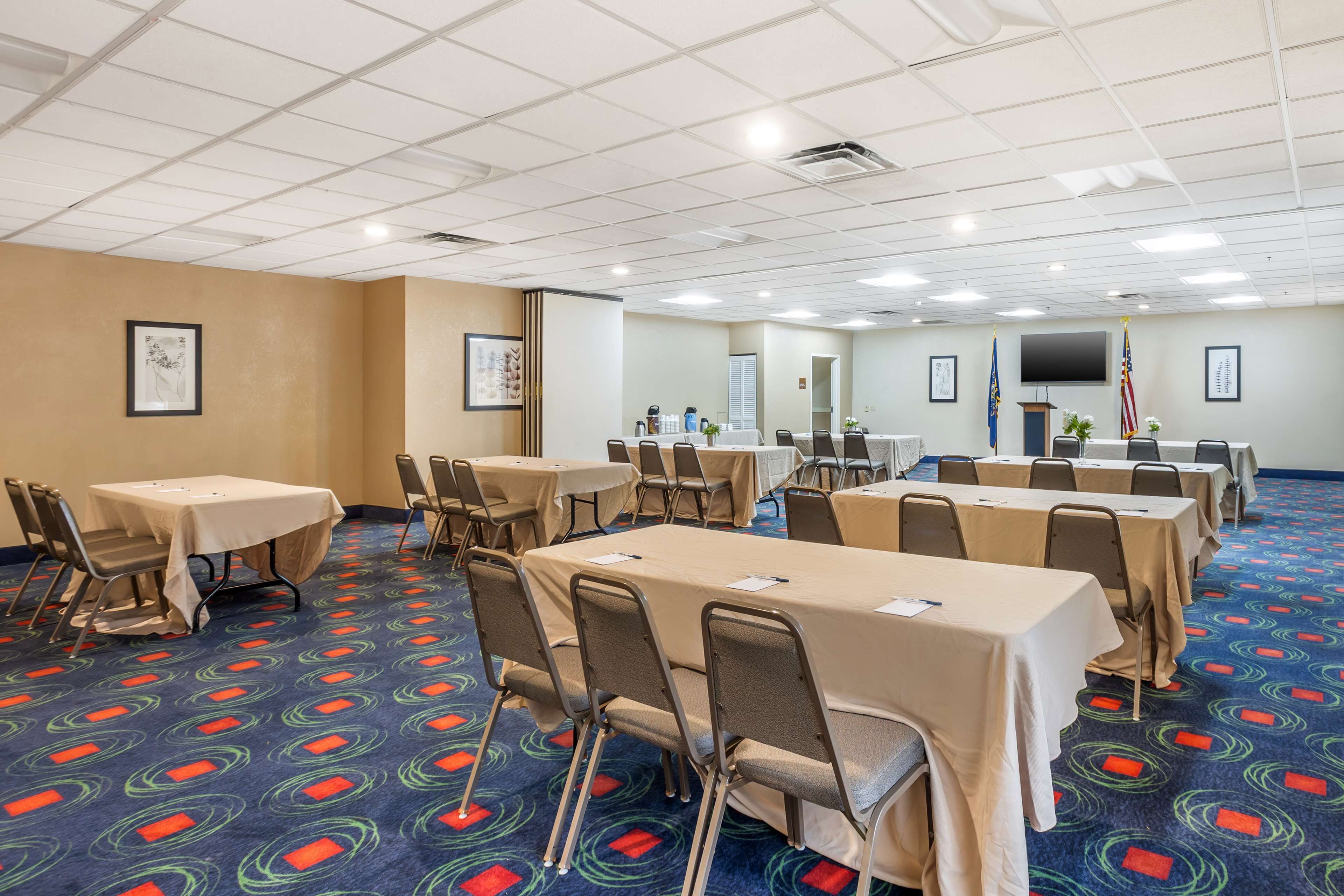 Une salle de conférence dotée de plusieurs tables et de chaises, d’un tapis à motifs et d’œuvres d’art encadrées accrochées aux murs.