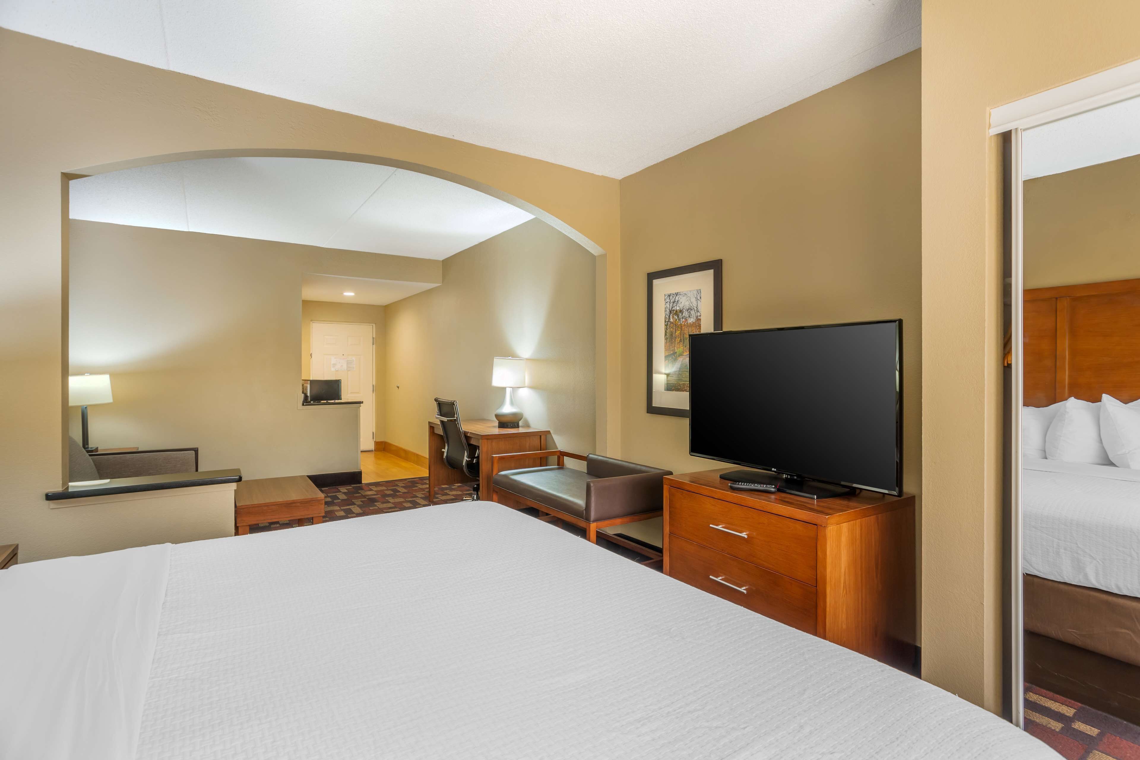Una habitación de hotel con una cama grande, televisión, escritorio con silla y una mesita.