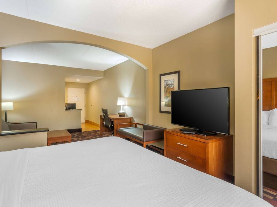 Ein Hotelzimmer mit einem großen Bett, einem Fernseher, einem Schreibtisch mit Stuhl und einem kleinen Tisch.