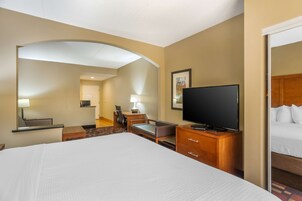 A hotel room with a large bed, a television, a desk with a chair, and a small table.