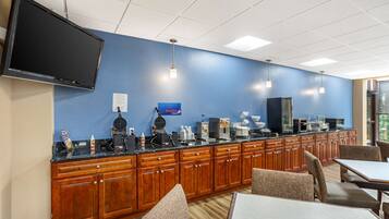 A hotel breakfast area with a long counter, wooden cabinets, and seating.