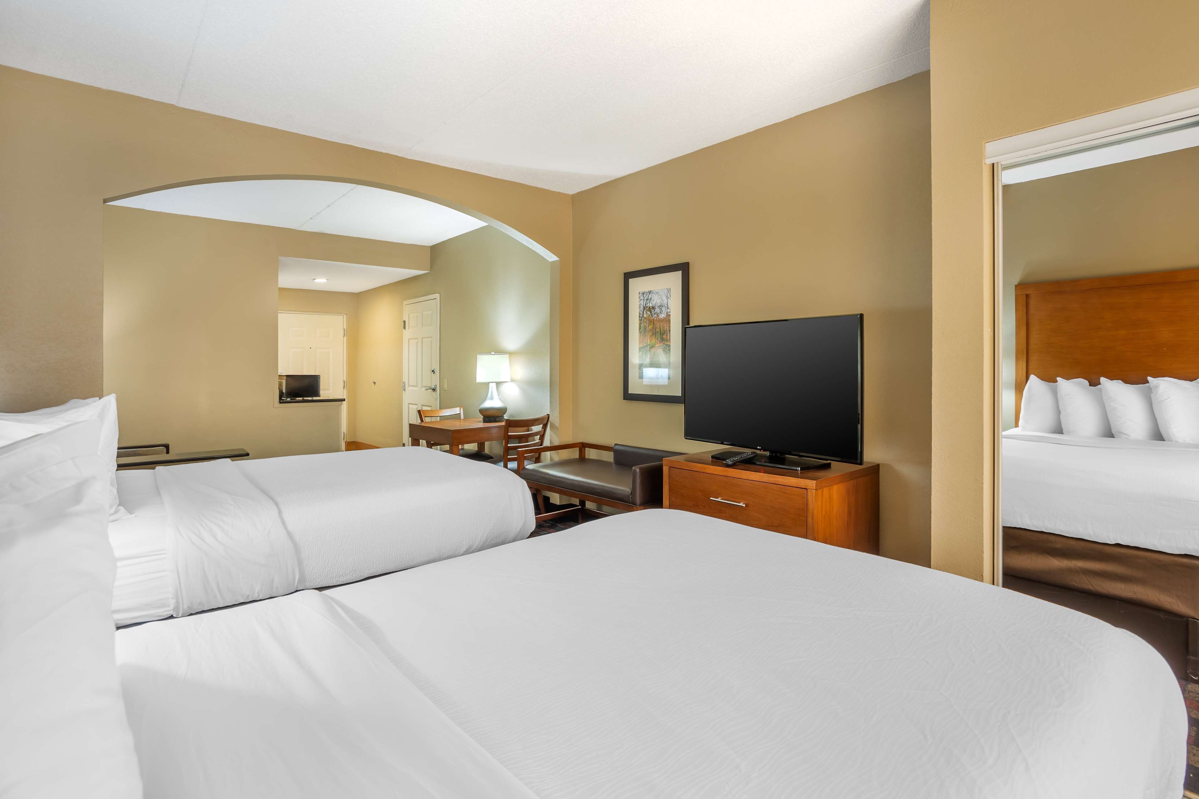 A hotel room with two beds, a desk with a chair, a television, and a mirror.