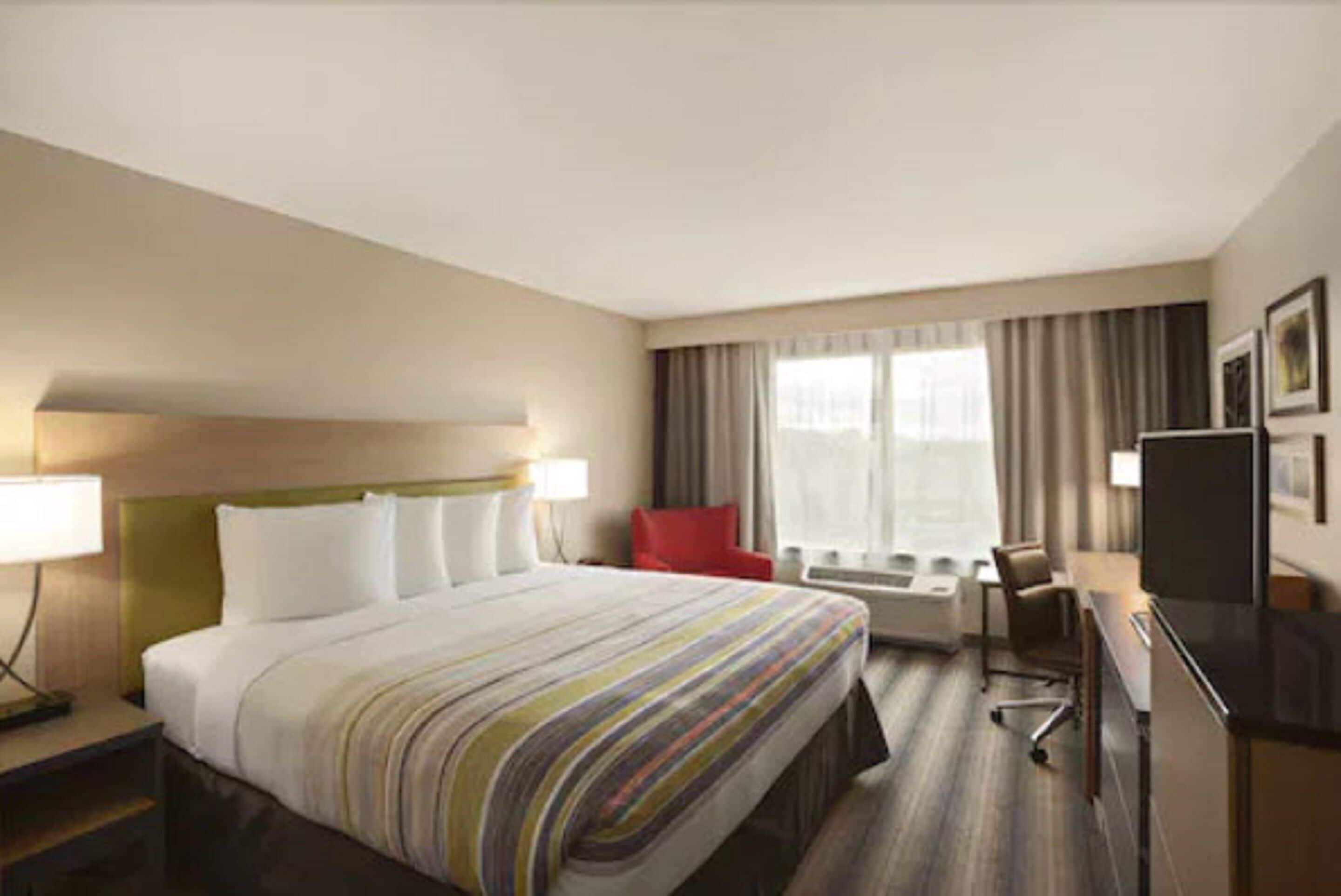 A hotel room with a bed, a desk, a chair, a TV, and a window with curtains.