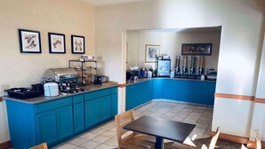 A small, modern kitchen with blue cabinets, a dining table with chairs, and a coffee machine. - Country Inn & Suites by Radisson, York, PA (York)