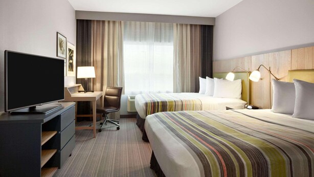 A hotel room with a TV, desk, two beds, a chair, and a large window with curtains. - Country Inn & Suites by Radisson, York, PA (York)