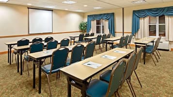 Una sala conferenze con diversi tavoli e sedie, uno schermo per proiettore e un'ampia finestra con tende.