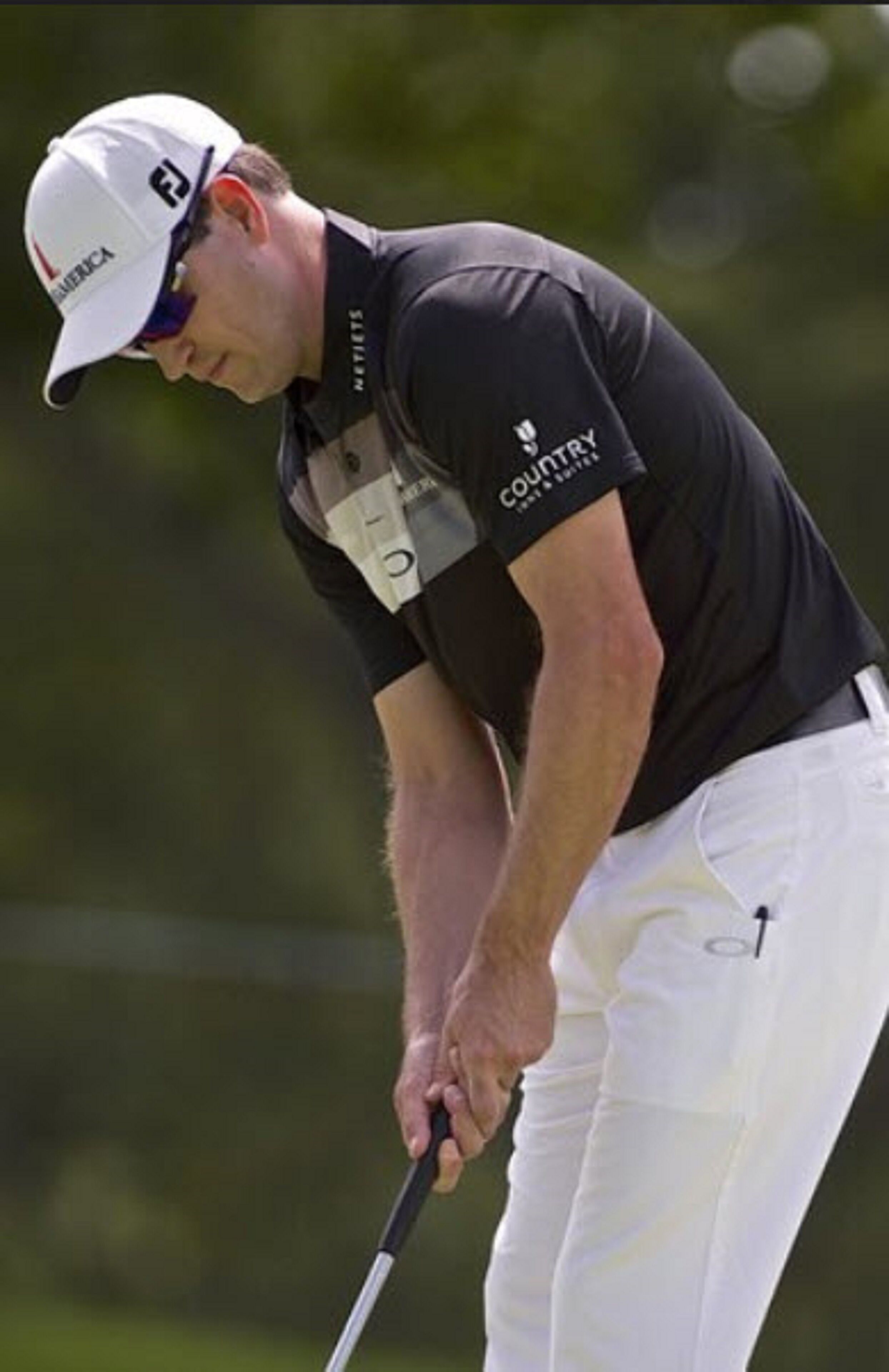 A golfer in a black shirt and white pants, holding a golf club.