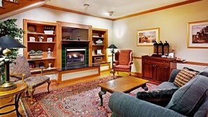 A cozy living room with a fireplace, wooden shelves, a red armchair, a blue sofa, and a patterned rug. - Country Inn & Suites by Radisson, York, PA (York)