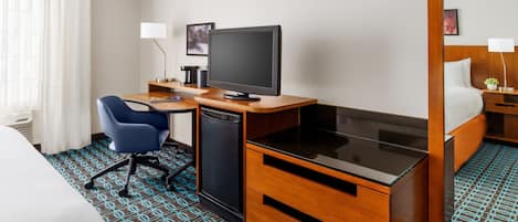 Ein Hotelzimmer mit einem Bett, einem Schreibtisch mit Computer, einem Sessel, einem kleinen Kühlschrank und einem Spiegel.
