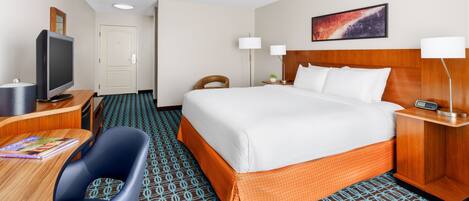 A hotel room with a large bed, a desk with a computer, a television, and a chair.