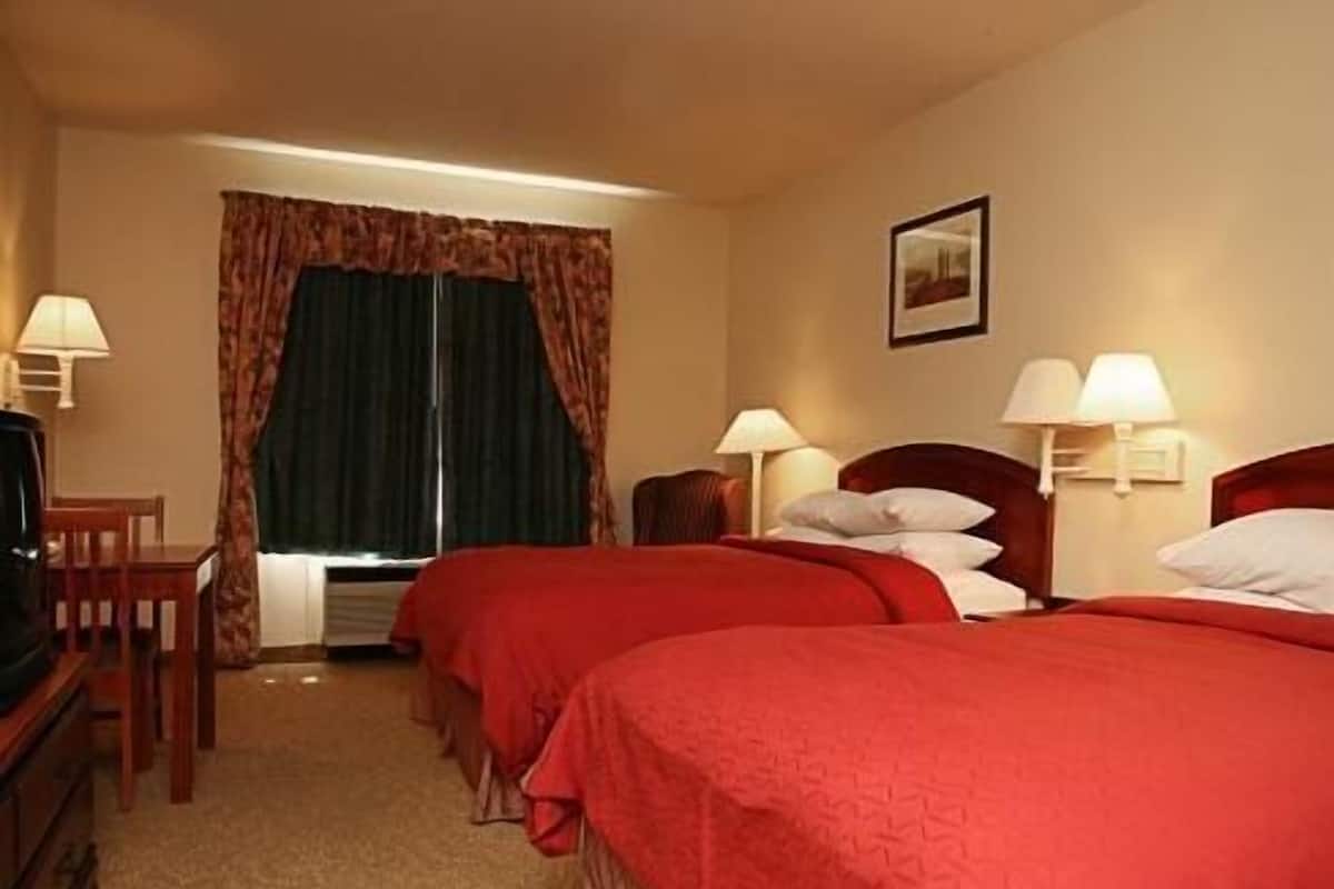 A hotel room with two beds, a desk, a chair, and a window with curtains.