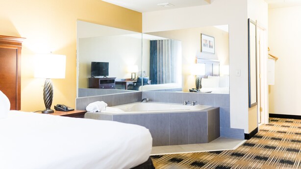 A hotel room with a large bed, a bathtub, a desk with a lamp, and a mirror reflecting the room. - Country Inn & Suites by Radisson, Helen, GA (Helen)