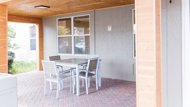 A covered patio with a brick floor, a table with chairs, and a window with blinds.