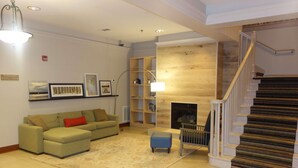 A living room with a sectional sofa, a fireplace, a staircase, and a bookshelf. - Country Inn & Suites by Radisson, Helen, GA (Helen)