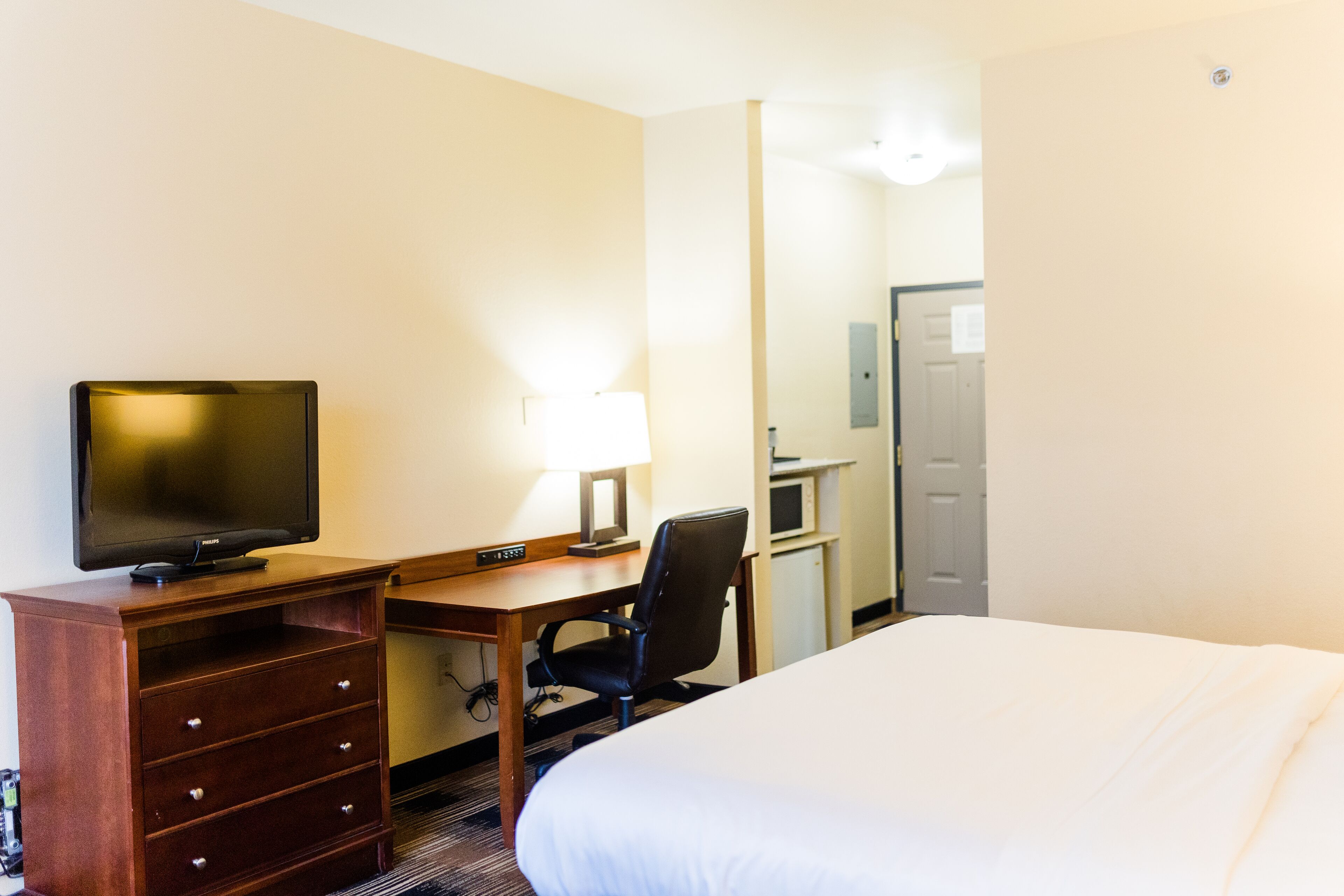 A hotel room with a bed, a desk with a computer and a lamp, a chair, and a television.