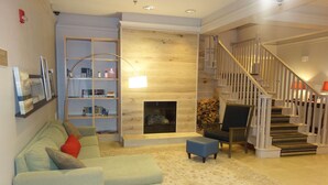 A living room with a sofa, ottoman, bookshelf, fireplace, and staircase. - Country Inn & Suites by Radisson, Helen, GA (Helen)