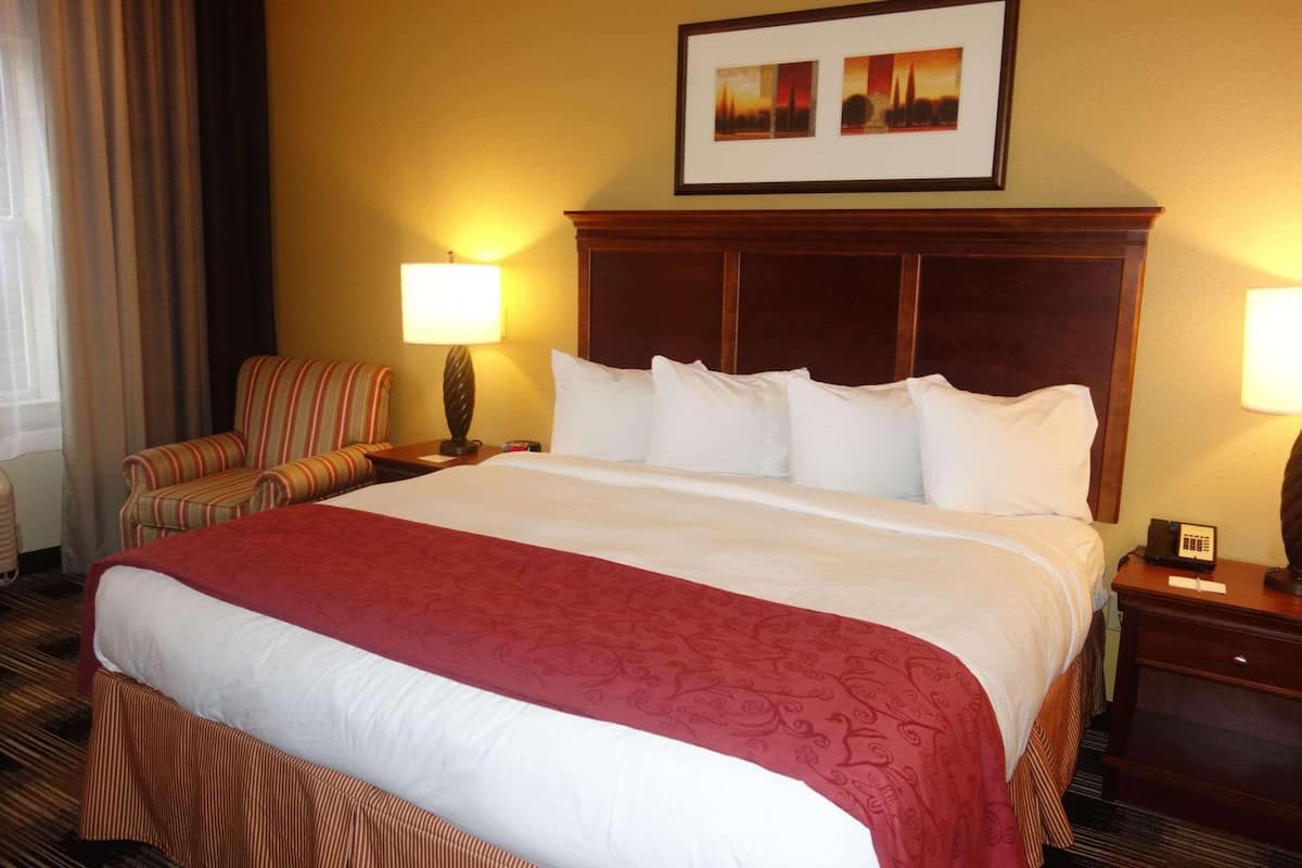 A hotel room with a large bed, two bedside lamps, a chair, and a framed picture on the wall.