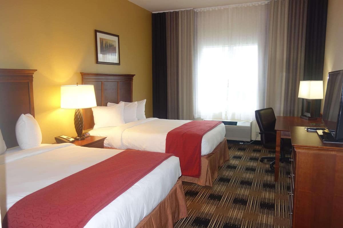 A hotel room with two beds, a desk, a chair, a TV, and a window with curtains.