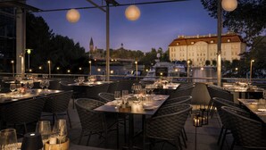 Un espace de restauration en plein air avec des tables et des chaises, des guirlandes lumineuses et une vue sur un bâtiment en arrière-plan.