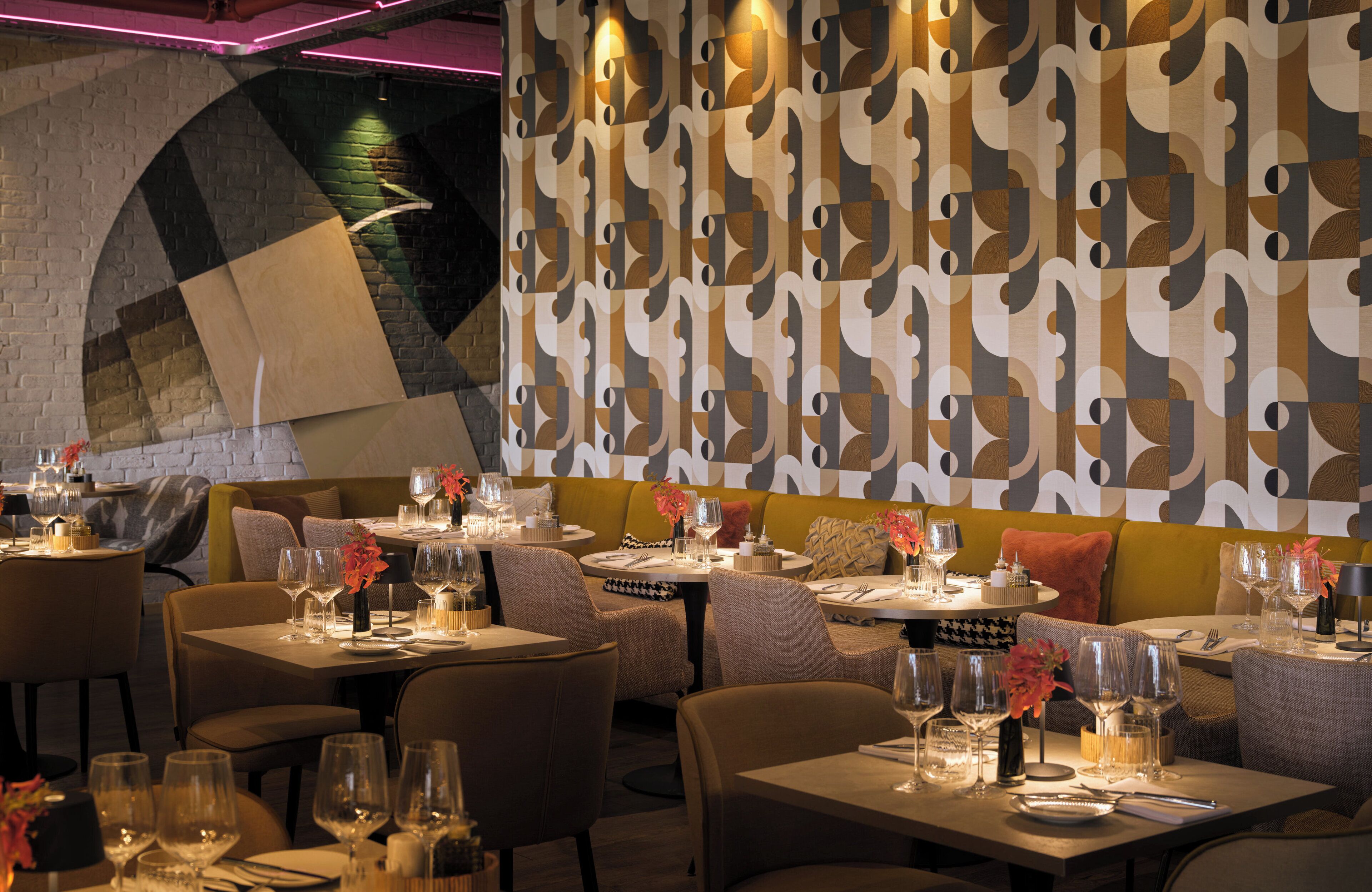 A restaurant with tables set for dining, featuring a patterned wall and a brick archway.