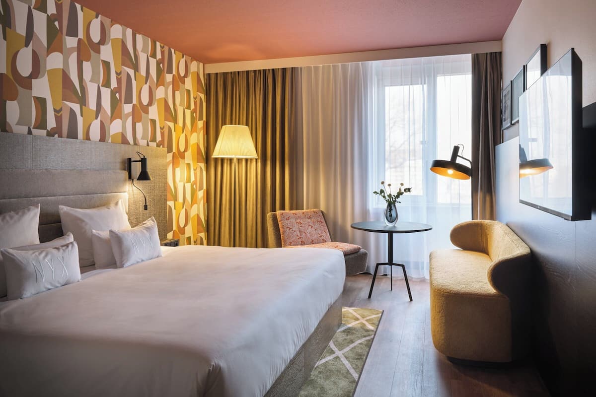 Una habitación de hotel con una cama grande, una silla, una mesita y una lámpara.