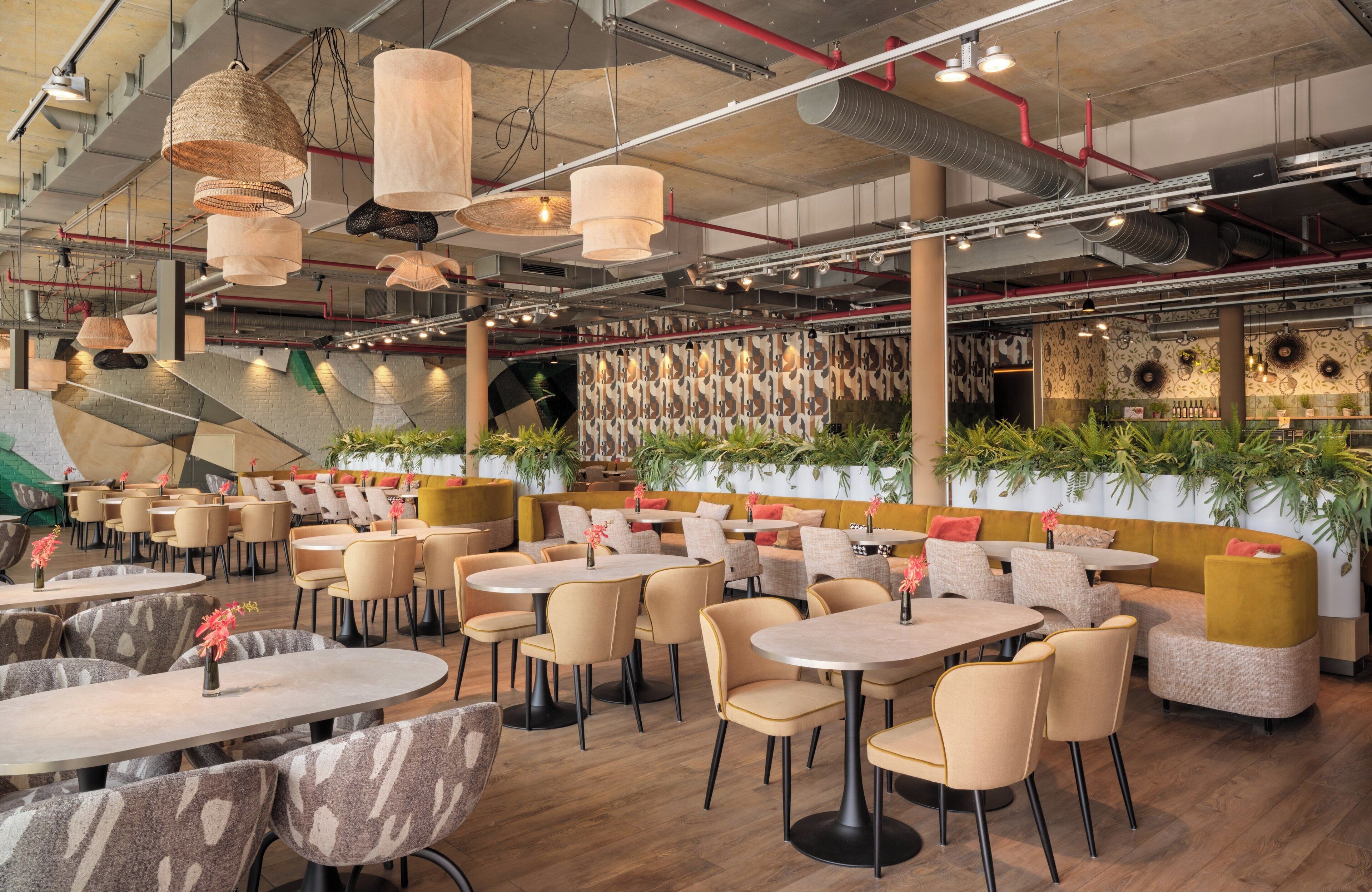 A spacious restaurant with multiple dining areas, including round tables and booths, and a variety of hanging light fixtures.