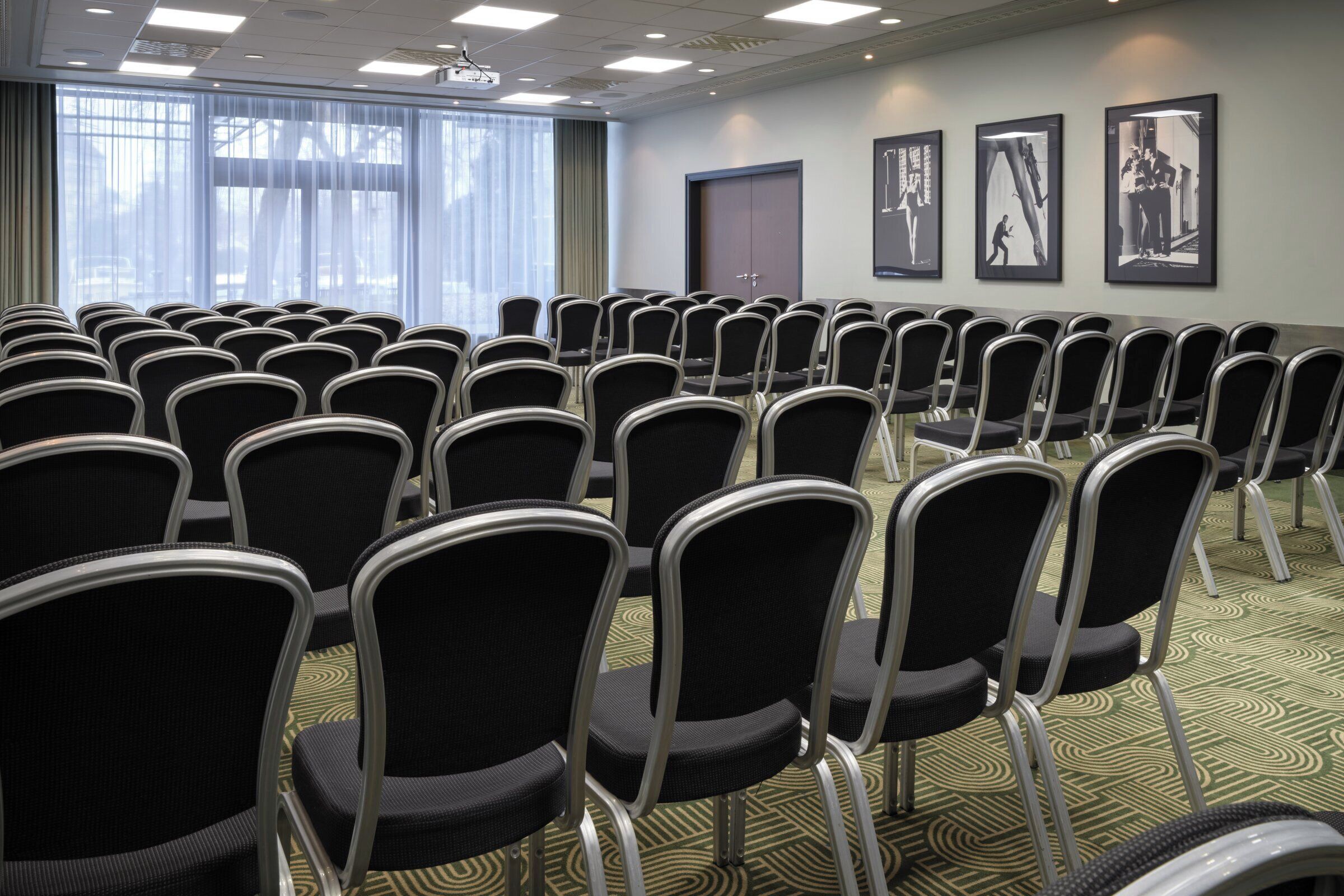 Un salón de conferencias con filas de sillas, un proyector y cuadros en la pared.