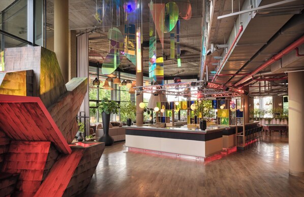 A modern bar area with a wooden counter, hanging lights, and a staircase with red accents.