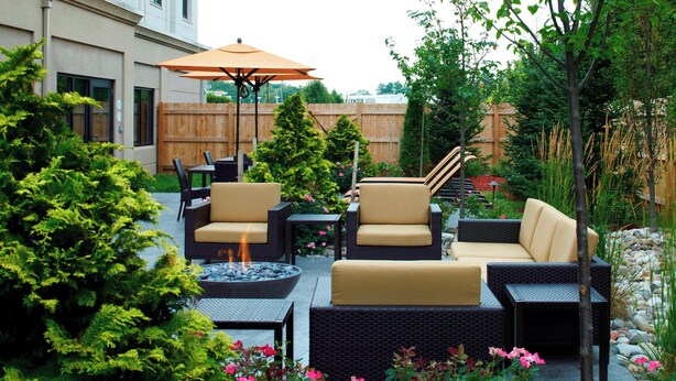 An outdoor patio with wicker furniture, a fire pit, and a wooden fence in the background. - Courtyard by Marriott Buffalo Amherst/University (Buffalo)