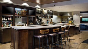 A modern bar area with a long counter, stools, and a variety of bottles and glasses. - Courtyard by Marriott Buffalo Amherst/University (Buffalo)